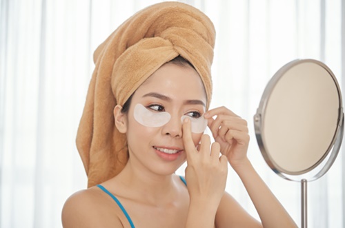 Mulher com bandagens debaixo dos olhos e toalha na cabeça se olhando no espelho