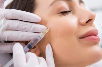 Profissional com luvas segurando uma seringa e aplicando ácido hialurônico no rosto de uma paciente, semelhante ao tratamento da clínica Teresa Noviello