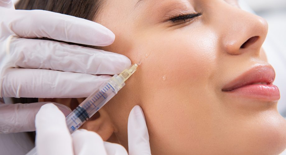Profissional com luvas segurando uma seringa e aplicando ácido hialurônico no rosto de uma paciente, semelhante ao tratamento da clínica Teresa Noviello