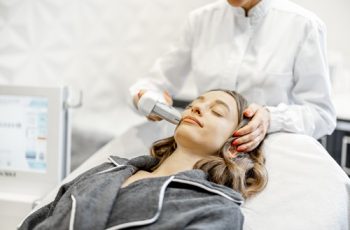 Mulher deitada recebendo tratamento no rosto com o ultrassom, como na clínica Teresa Noviello